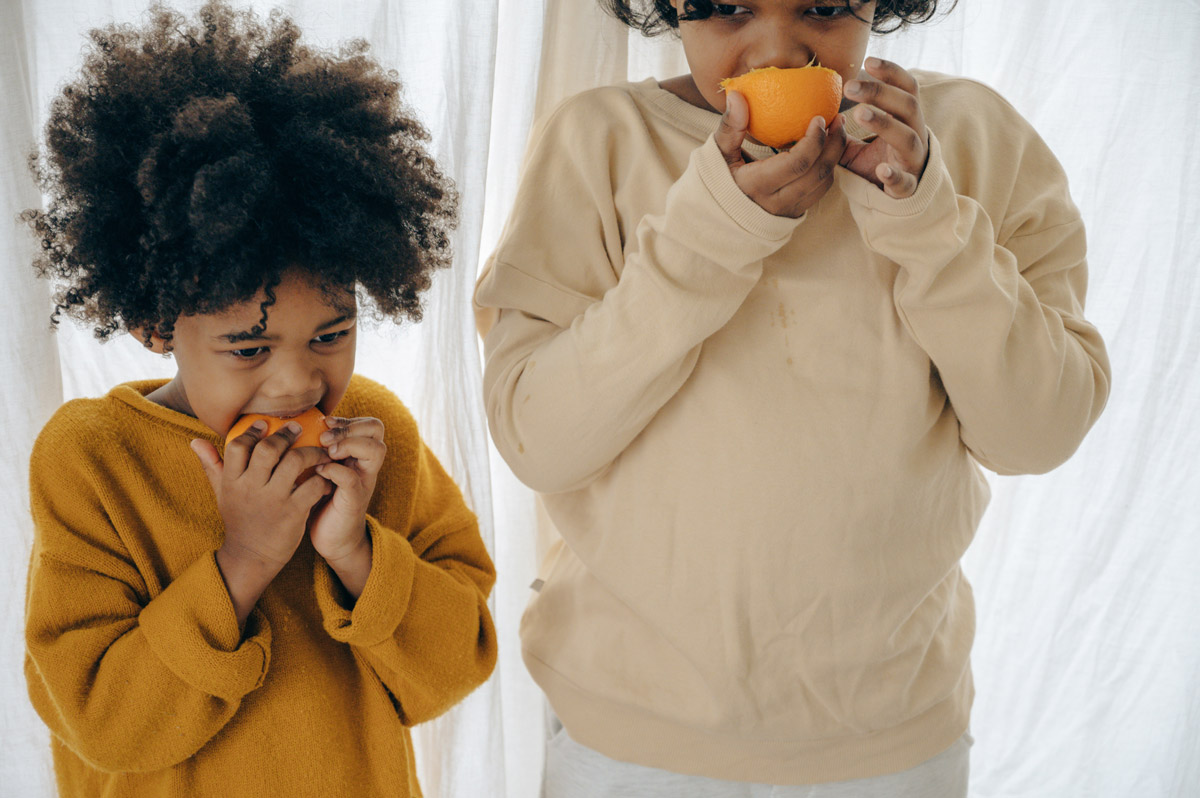 Two children bite into orange halves to prevent flu
