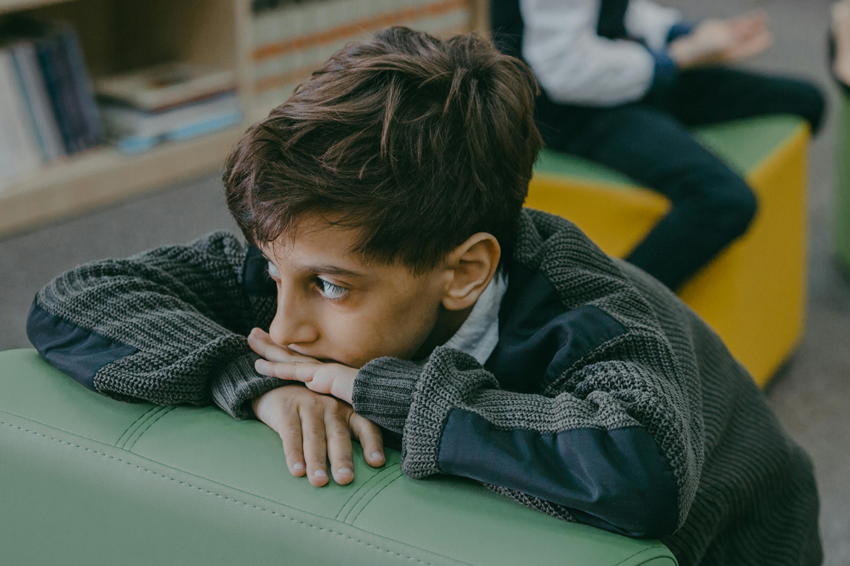 young boy rests his head on his hands and looks pensively off-camera